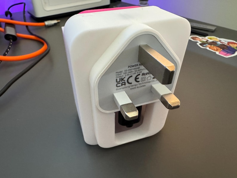 May include: White power adapter with a UK three-pin plug. The adapter has a label that reads "POWER ADAPTER" and includes the following information: Model: 10-2000000000, Input: 100-240V~ 50/60Hz 0.3A, Output: 5.0V 1.0A, RoHS, UK CA CE. The adapter is made in China.