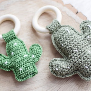 May include: Two crocheted cactus toys with wooden teething rings. The cactus toys are green with white stitching and the rings are natural wood.
