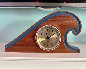 May include: A wooden clock shaped like a wave with a blue trim. The clock face is white with black numbers and hands. The clock says "Quartz" on the face.