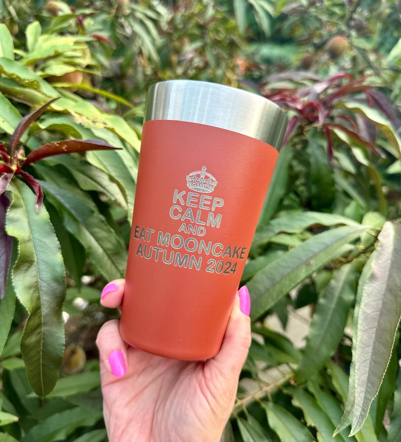 以下が含まれることがあります： 銀色の蓋が付いたさび色のステンレス製のタンブラー。タンブラーには「Keep Calm and Eat Mooncake Autumn 2024」という文字が刻まれています。