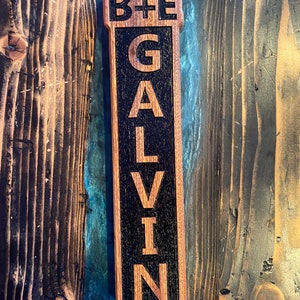 May include: A wooden bottle opener with a black background and the text "B+E GALVIN" engraved in white.