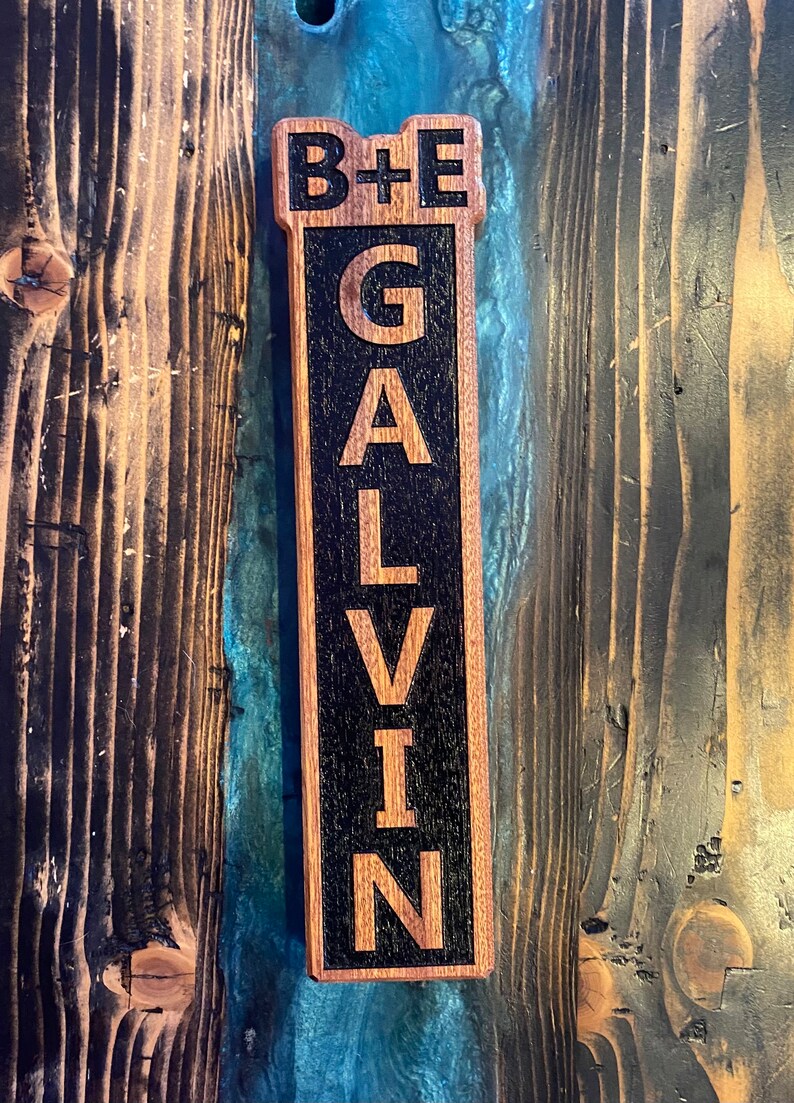 May include: A wooden bottle opener with a black background and the text "B+E GALVIN" engraved in white.