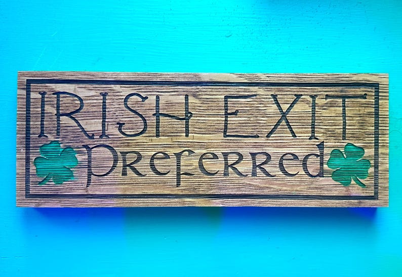 K&ouml;nnte beinhalten: Rechteckiges Holzschild mit dem Text "IRISH EXIT Preferred" eingeritzt. Das Schild hat gr&uuml;ne Kleeblatt-Details und einen dunklen Rahmen. Der Hintergrund ist in einem hellen T&uuml;rkis gehalten.