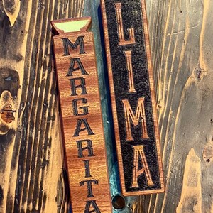 May include: Two wooden signs with the words "Margarita" and "Lima" engraved on them. The signs are both dark brown with black lettering.