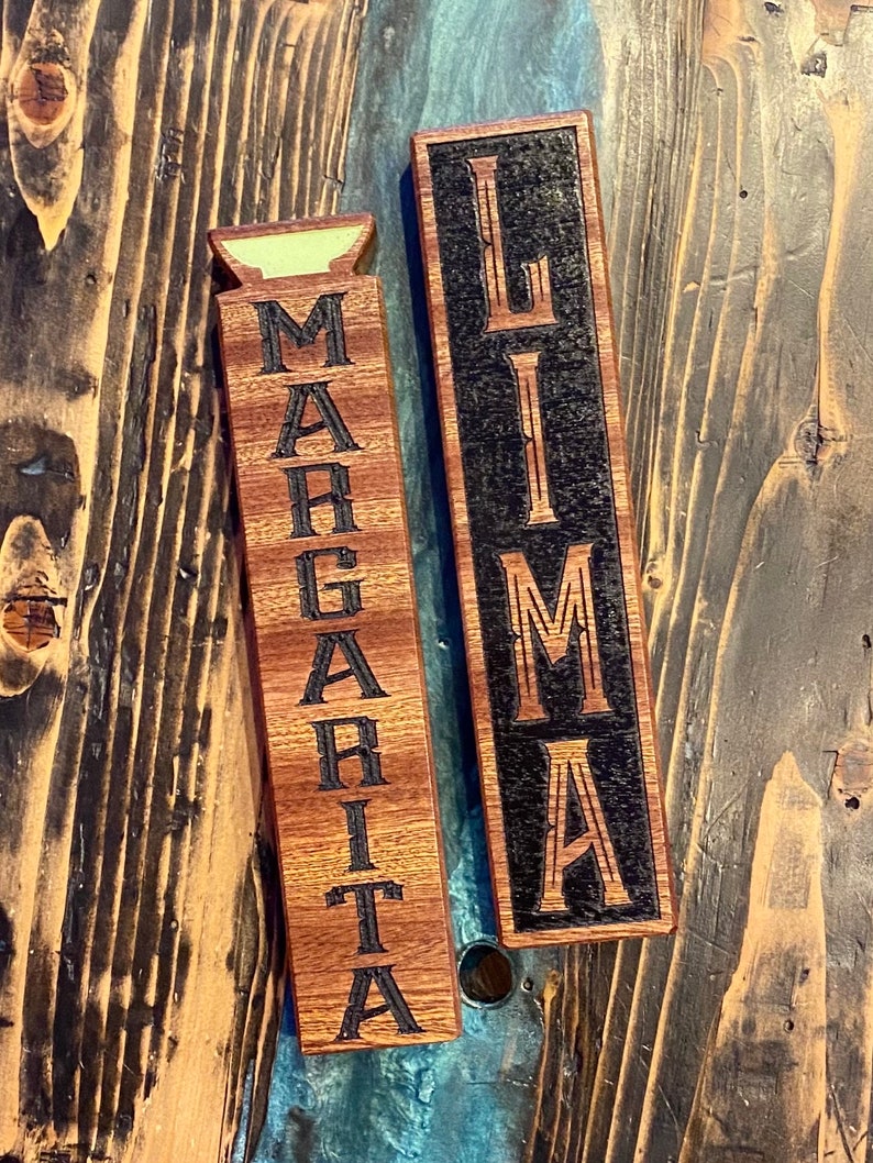 May include: Two wooden signs with the words "Margarita" and "Lima" engraved on them. The signs are both dark brown with black lettering.
