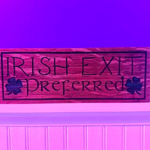 K&ouml;nnte beinhalten: Rechteckiges Holzschild mit den Worten "IRISH EXIT PREFERRED" in schwarzer Schrift. Das Schild hat einen dunklen Rand und zeigt auf jeder Seite ein Kleeblatt. Das Holz hat eine rotbraune Beize.