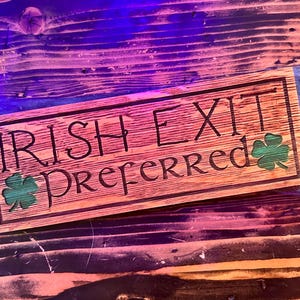 K&ouml;nnte beinhalten: Rechteckiges Holzschild mit dem eingravierten Text "IRISH EXIT PREFERRED". Das Schild hat zwei gr&uuml;ne Kleebl&auml;tter. Das Holz hat eine nat&uuml;rliche Maserung und ist hellbraun gebeizt.
