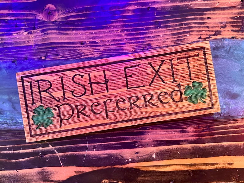 K&ouml;nnte beinhalten: Rechteckiges Holzschild mit dem eingravierten Text "IRISH EXIT PREFERRED". Das Schild hat zwei gr&uuml;ne Kleebl&auml;tter. Das Holz hat eine nat&uuml;rliche Maserung und ist hellbraun gebeizt.