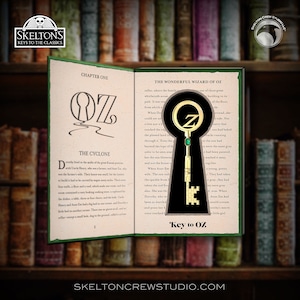 May include: A gold-colored key with a green jewel on the top, shaped like the letter "O" with a swirl at the bottom. The key is on a page from the book "The Wonderful Wizard of Oz" with the text "Key to Oz" below it.