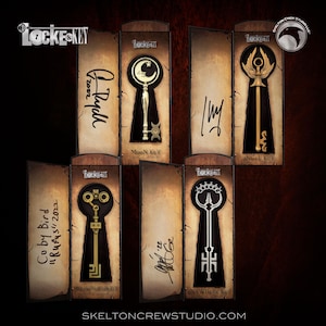 May include: Five decorative key-shaped items displayed in individual boxes. Each box features a different key design, including a moon key, an angel key, a key with a crown, and a key with a gear design. The boxes are all made of a brown paper-like material and have a vintage look.