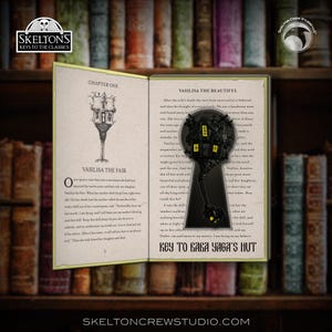 Puede incluir: Un objeto decorativo en forma de ojo de cerradura con un diseño de casa en miniatura, con una combinación de colores oscuros con acentos amarillos. El ojo de cerradura está colocado sobre un libro abierto con texto, y las palabras "Key to Baba Yaga's Hut" son visibles.