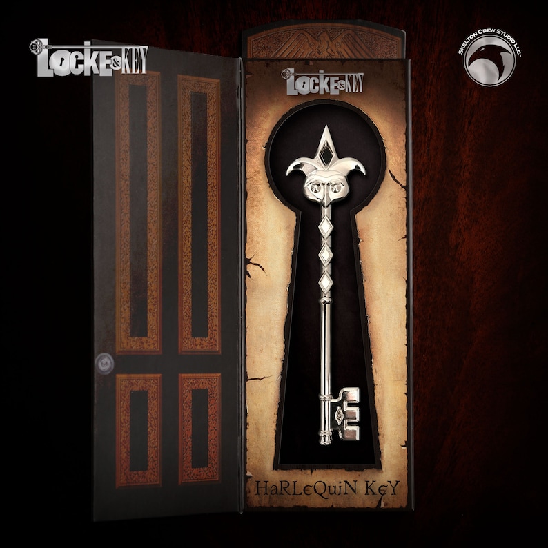 Pu&ograve; includere: Una chiave d'argento con un design a testa di giullare, esposta in una scatola nera e marrone con le parole "Locke & Key" e "Harlequin Key".