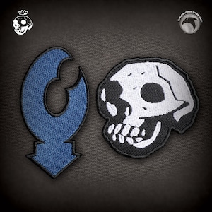 Puede incluir: Dos parches bordados, uno azul y con forma de flecha hacia abajo, el otro blanco y negro con un diseño de calavera.