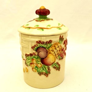 May include: A ceramic jar with a lid decorated with a basket weave pattern and a colourful fruit design. The lid has a flower-shaped knob.