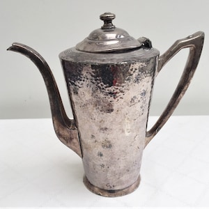 May include: A silver teapot with a hammered finish and a lid with a knob. The teapot has a spout and a handle.