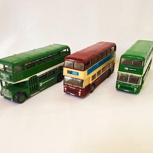 May include: Three miniature double-decker buses in green, red, and yellow. The green buses have white stripes and the red bus has a yellow stripe. The buses have windows and detailed features. One bus has the text "Eastern National" and another has the number "108".
