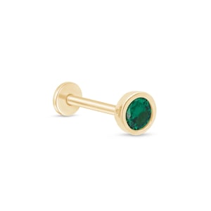 May include: Gold body piercing with a small emerald green gemstone.
