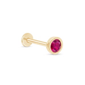May include: A gold stud earring featuring a vibrant red gemstone. The earring has a flat back and a post for piercing. The round gemstone is set within a bezel setting.
