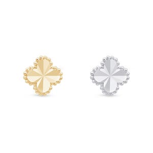 May include: Two four-leaf clover shaped studs, one in polished yellow gold and one in polished silver tone metal. Each stud features a faceted surface with a central star-like pattern and a beaded border edge, creating a distinct textured outline.