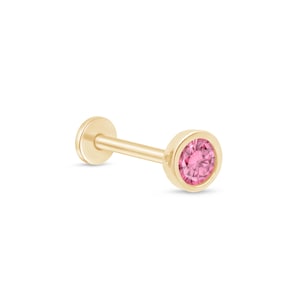 Puede incluir: Un piercing de cuerpo de oro con una pequeña piedra preciosa rosa. El piercing es un pendiente con una parte posterior plana y una parte superior redonda.