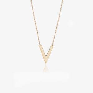 Könnte beinhalten: Eine goldfarbene Halskette mit einem V-förmigen Anhänger. Der Anhänger hat ein solides, flaches Design, und die Kette ist filigran. Die Halskette wird vor einem weißen Hintergrund mit einer dezenten Reflexion darunter präsentiert.