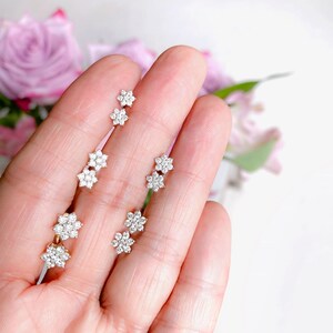 a person holding three flower shaped earrings in their hand