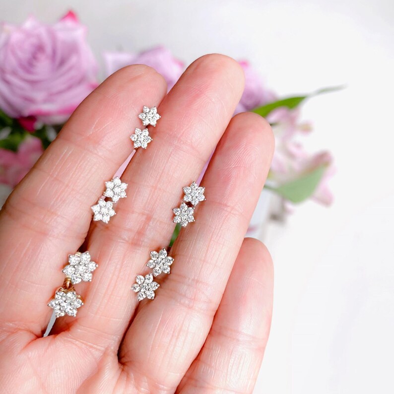 a person holding three flower shaped earrings in their hand