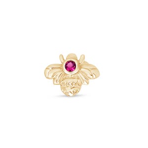 May include: Gold bee charm with a pink gemstone in the center. The bee is detailed with wings and a body.