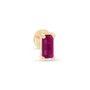 May include: A single gold-colored earring with a rectangular, deep pink gemstone. The earring has a flat, round backing and four rounded prongs securing the gemstone. The gemstone is a vibrant, saturated pink color.