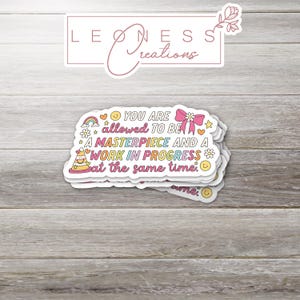 May include: A sticker with a rainbow, stars, and smiley faces. The text reads "You are allowed to be a masterpiece and a work in progress at the same time."