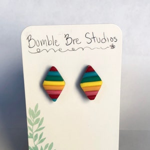 Può includere: Un paio di orecchini colorati a forma di diamante con un motivo a strisce arcobaleno. Gli orecchini sono su una carta bianca con il testo "Bumble Bre Studios" scritto su di essa.