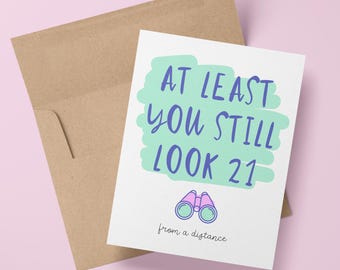Puede incluir: Una tarjeta blanca con un diseño verde y azul. El texto en la tarjeta dice "Al menos todavía te ves de 21 años desde la distancia". Una ilustración rosa y morada de binoculares está debajo del texto.