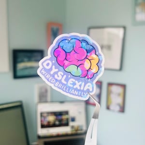 Puede incluir: Una pegatina holográfica con un diseño de cerebro colorido y el texto "Dislexia Conectado Brillantemente".