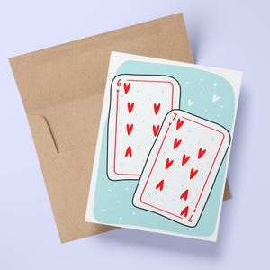 May include: A greeting card featuring illustrations of playing cards, the six and seven of hearts, with a light blue background and small white hearts. The card is paired with a brown envelope.