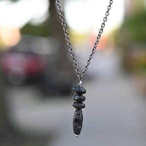 May include: A silver chain necklace with a pendant made of three stacked black lava rock beads.