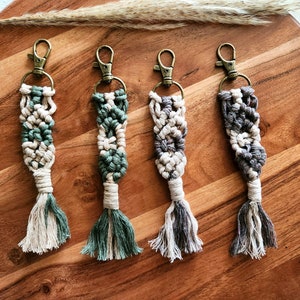 May include: Four handmade macrame keychains with a tassel. The keychains are in shades of beige, green, and gray.