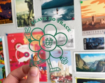 May include: A green and white sticker with a cartoon flower character holding up two fingers in a peace sign. The flower has a smiling face and the text "LEAVE NO TRACE" is written above it.