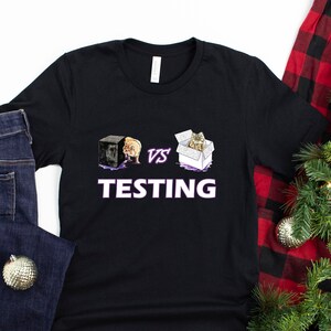 May include: Black t-shirt featuring a graphic of two boxes, one with a cat and the other with a dog, and the text "VS TESTING" in purple.