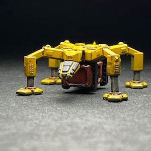 May include: A yellow and black toy robot with six legs and a cargo container. The robot is made of plastic and has a detailed design.