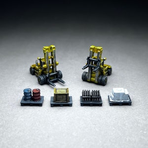 May include: Two yellow toy forklifts with black forks, one facing forward and one facing backward, are positioned on a gray surface.  The forklifts are surrounded by five pallets with various cargo, including barrels, crates, and a block of concrete.