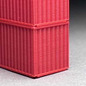 May include: Close-up of a red corrugated cardboard box. The box is made of thick cardboard and has a textured surface.