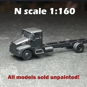 May include: A matte black N scale 1:160 model truck chassis featuring a cab, side mirrors, and dual rear wheels. The text N scale 1:160 and All models sold unpainted! is visible in the image. This miniature vehicle is presented as a single unit.