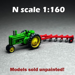 May include: Green and yellow toy tractor with a red plow attached. The tractor is labeled "N scale 1:160". The text "Models sold unpainted!" is at the bottom of the image.