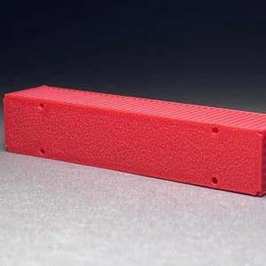 May include: A red plastic model of a shipping container. The container has a textured surface and is about 10 inches long.