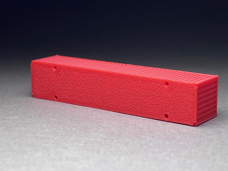 May include: A red plastic model of a shipping container. The container has a textured surface and is about 10 inches long.