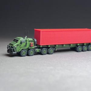 May include: A green military truck with a red shipping container on a flatbed trailer. The truck has a large front bumper and a small cab. The container is empty and has a metal door on one side.