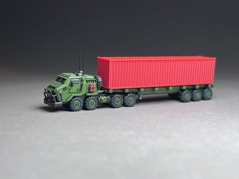 May include: A green military truck with a red shipping container on a flatbed trailer. The truck has a large front bumper and a small cab. The container is empty and has a metal door on one side.