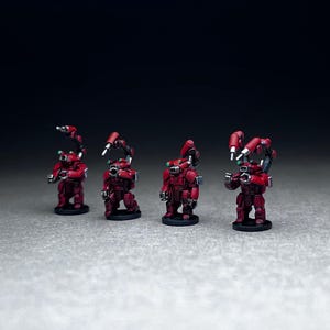May include: Four red and silver miniature robots with articulated arms and legs. The robots are posed in a line, facing forward.