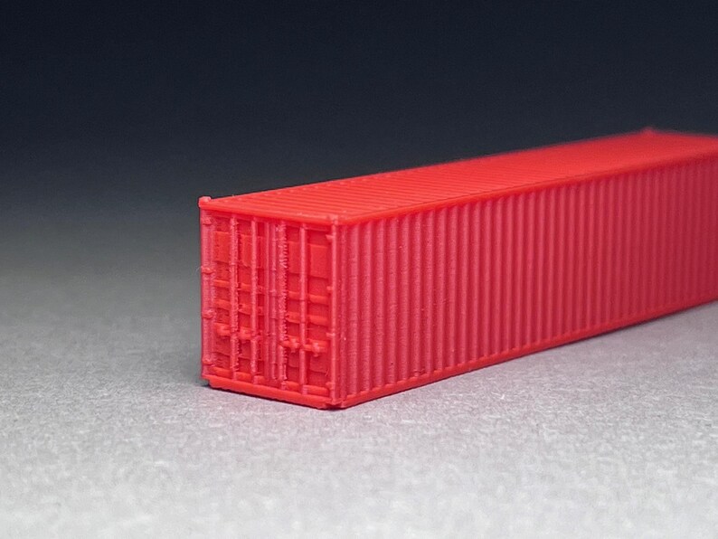 May include: A red shipping container model. The container is made of plastic and has a corrugated texture. The container is about 10 inches long.