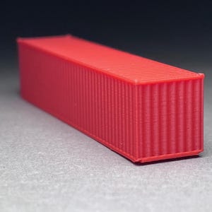 May include: A red shipping container model. The container is made of plastic and has a corrugated texture.